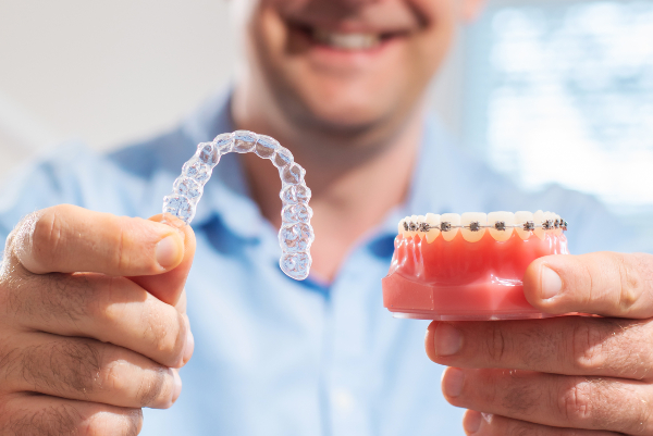 Uomo mostra Invisalign®, l'allineatore dentale trasparente, e un apparecchio tradizionale metallico